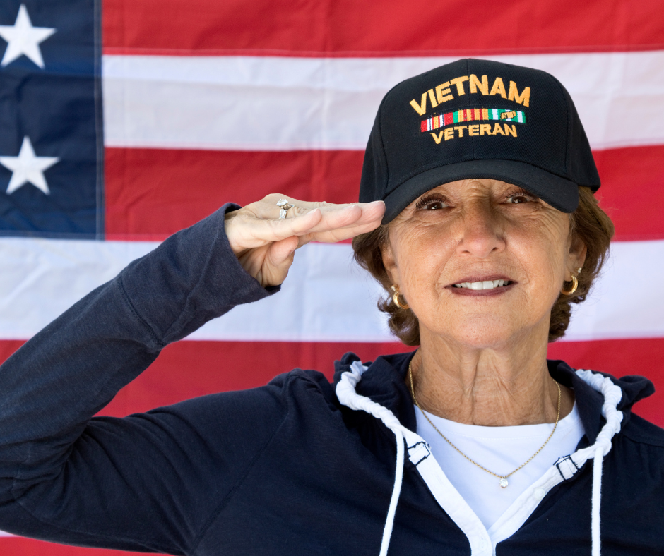 Woman with vietnam veteran hat saluting in front of american flag